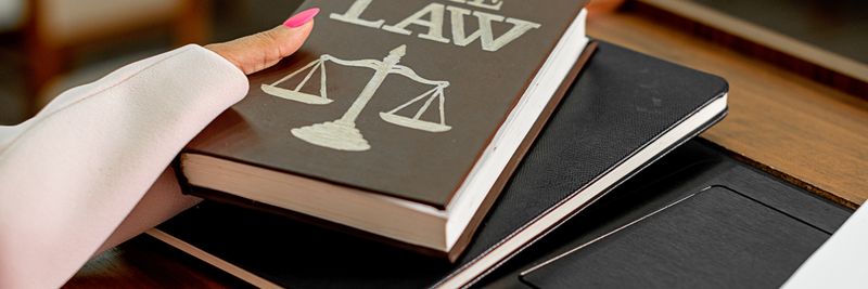 Closeup image of a law book titled 'The Law' on a wooden desk with scales of justice.