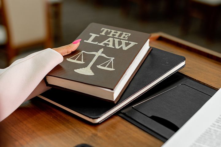 A hand resting on a law book with a scales of justice on its cover, on a desk