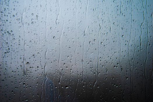 Rain-covered window with visible droplets and streaks creating a textured surface and moody ambiance.
