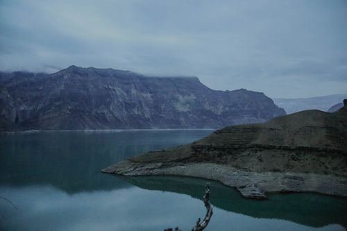 Free Serene twilight view of a misty mountain lake with reflective waters and dramatic mountains. Stock Photo