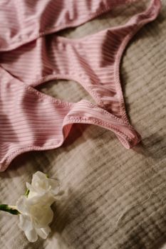 A pink ribbed undergarment lying on a textured fabric surface beside a white flower.