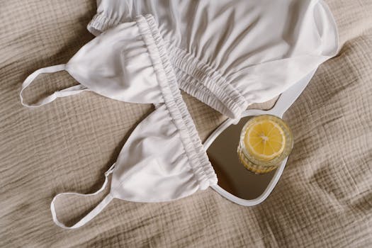 Close-up of white lingerie with a refreshing drink on a mirror atop a beige fabric.