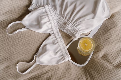 Free Close-up of white lingerie with a refreshing drink on a mirror atop a beige fabric. Stock Photo