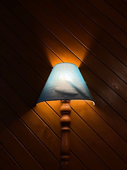 Free A classic vintage wooden table lamp with a blue shade against a dark wood plank wall. Stock Photo