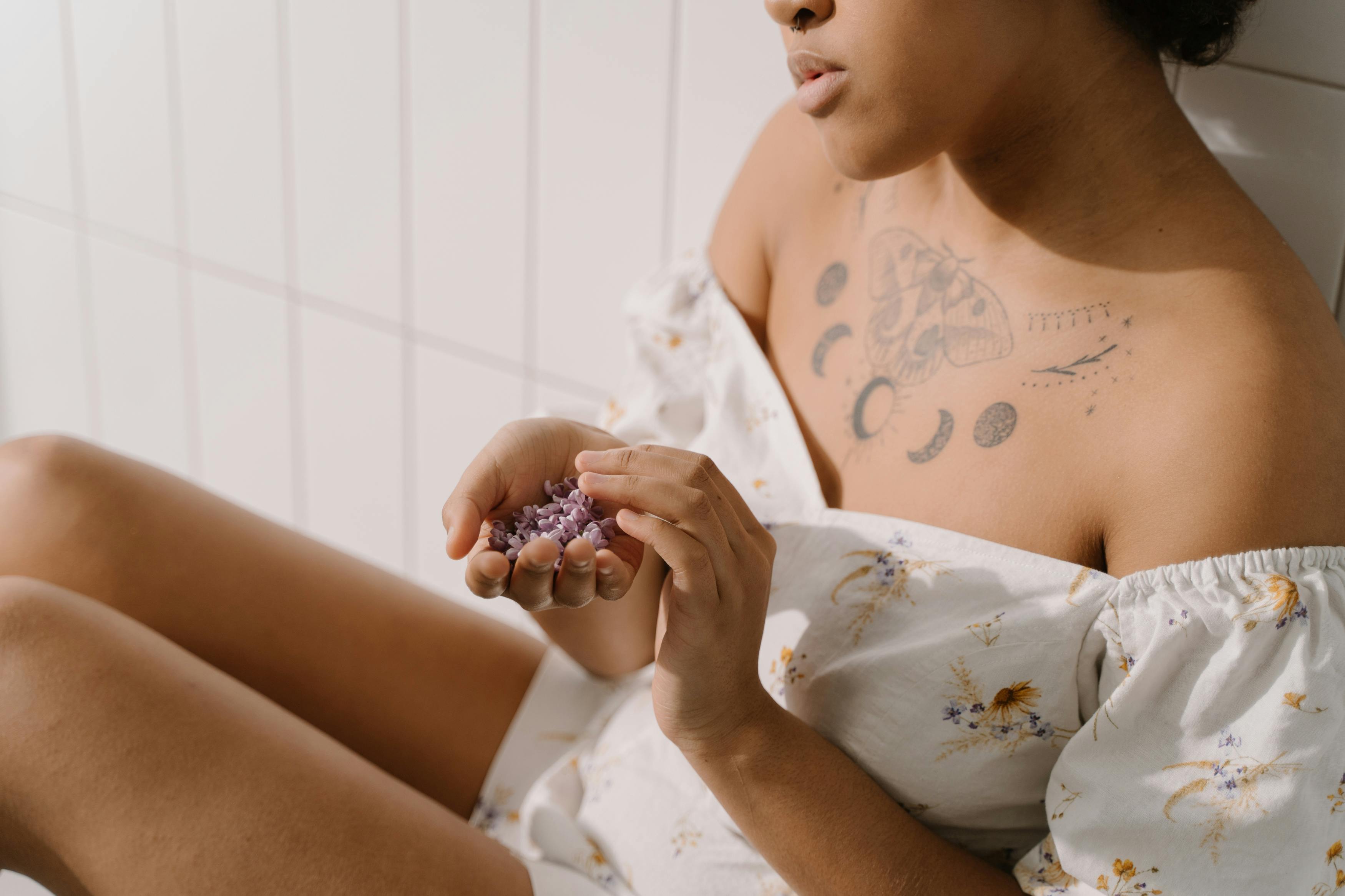 Tattooed woman in a floral dress holding purple crystals indoors. Relaxed mood.
