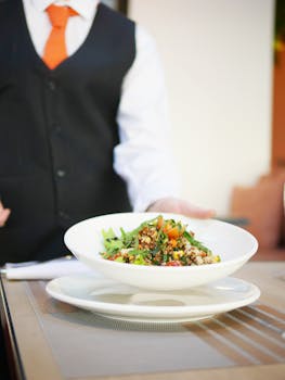 Quinoa salad in a bowl served by a waiter in a formal setting, highlighting fresh ingredients.