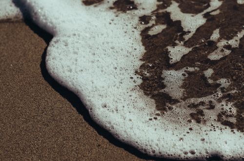 Free Close-up of sea foam gently washing over a sandy beach, capturing the serene coastal ambiance. Stock Photo