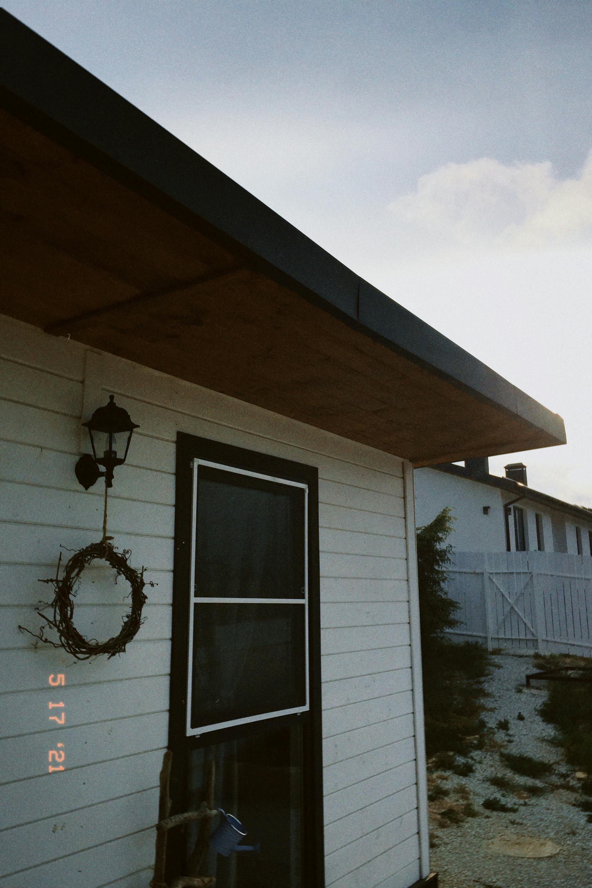 Cozy rustic house exterior featuring a wreath and outdoor lamp.