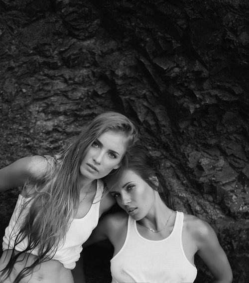 Free Artistic black and white portrait of two women posing in white tank tops against a rocky background. Stock Photo