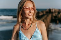 海边阳光明媚的海滩上，一名戴着墨镜和比基尼的女子微笑着