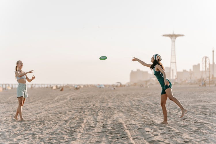 Two Women Playing Frisbee On The Beach