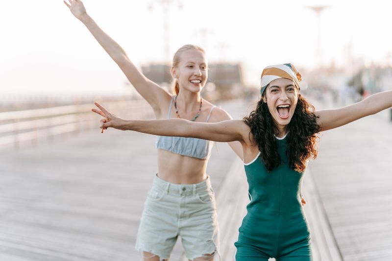 Two young women joyful and carefree on a sunny boardwalk.