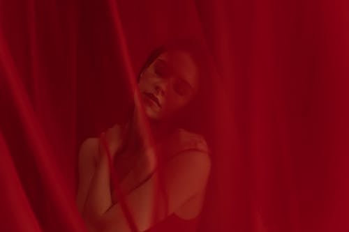 
A Woman in a Sleeveless Top behind a Red Curtain