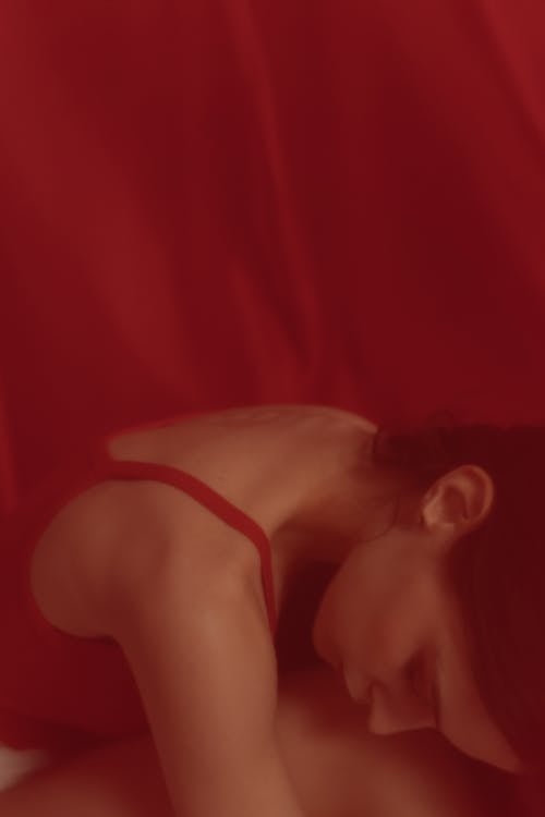 A Woman in Red Spaghetti Strap Top Resting her Face on Knees
