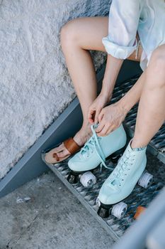 Close-up of a woman tying aqua roller skates while sitting on outdoor stairs, ready for skating.