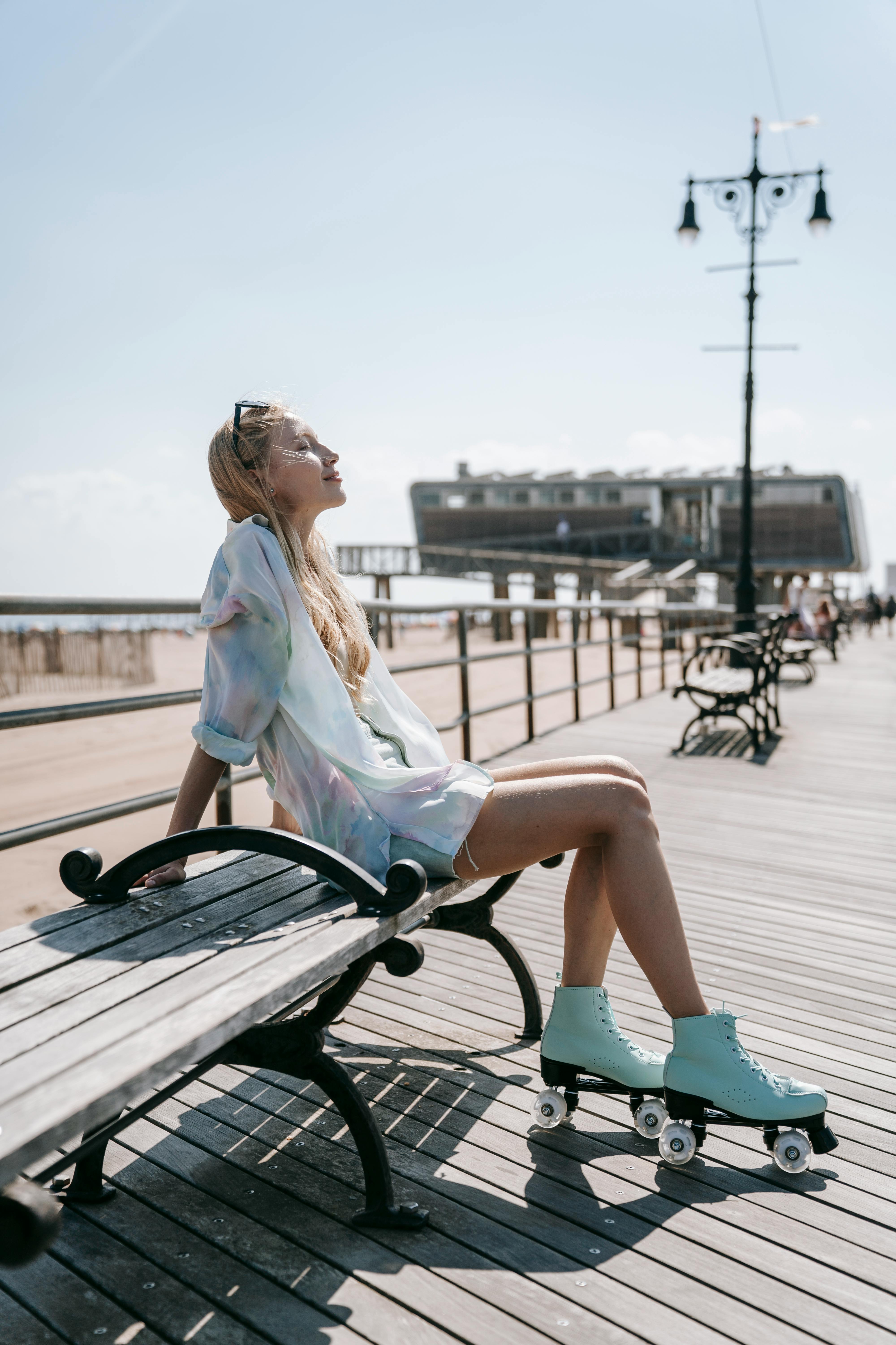 A woman sits on a bench with roller skates, enjoying the sunny boardwalk.