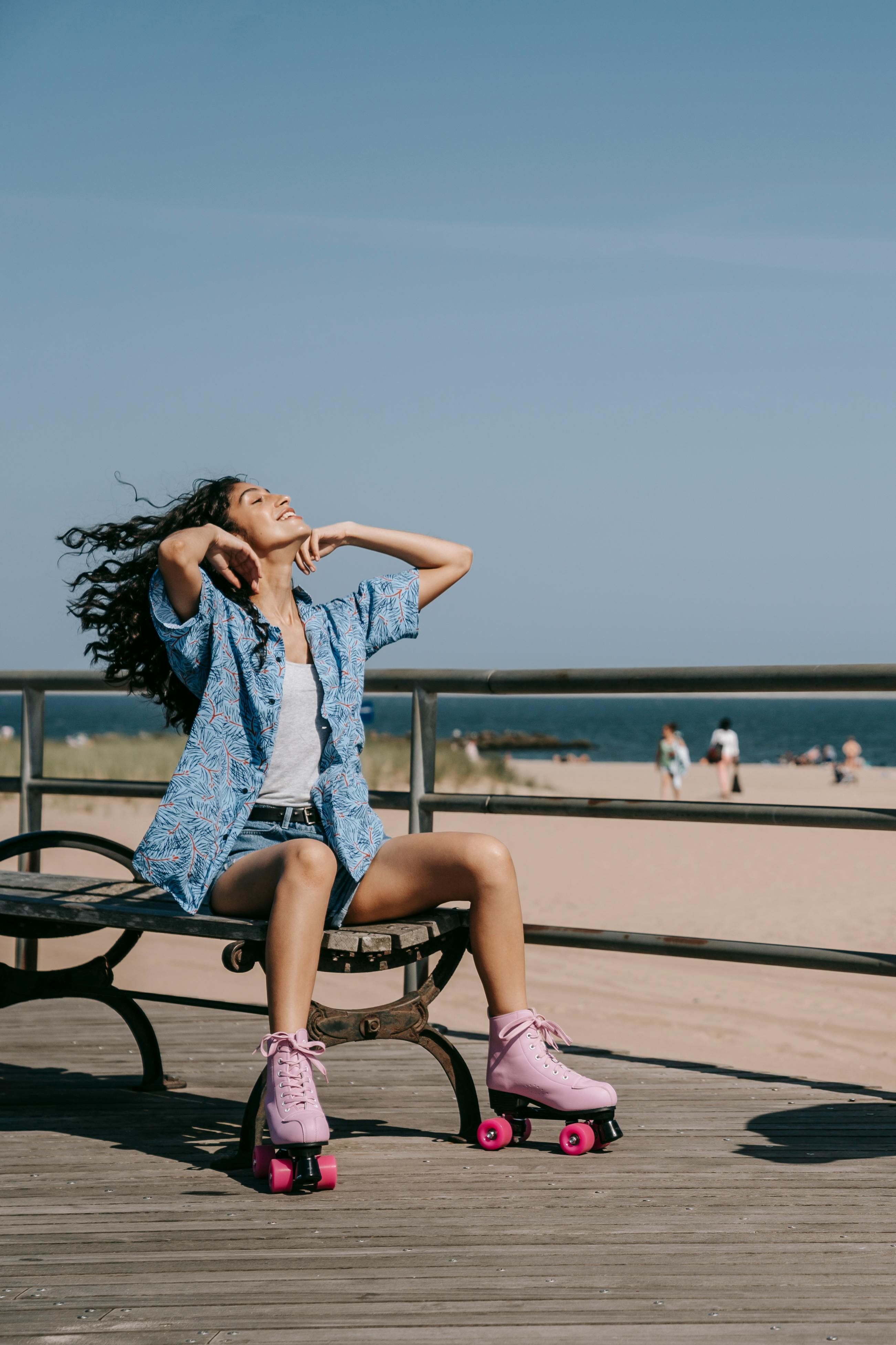 穿着粉色轮滑鞋的女子在阳光明媚的海滨木板路上的长凳上放松身心