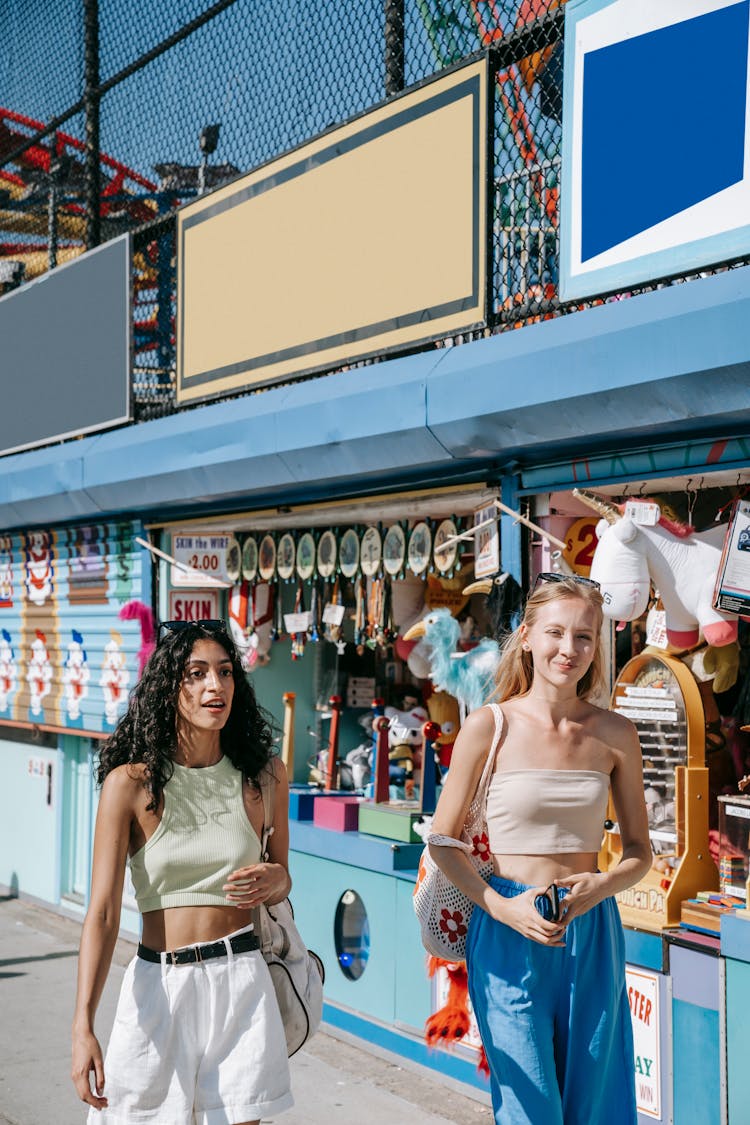 Young Women Walking On A Sidewalk Beside A Beach Market 