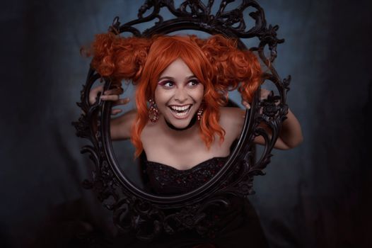 A lively portrait of a woman with orange hair posing through a decorative black frame, captured indoors.
