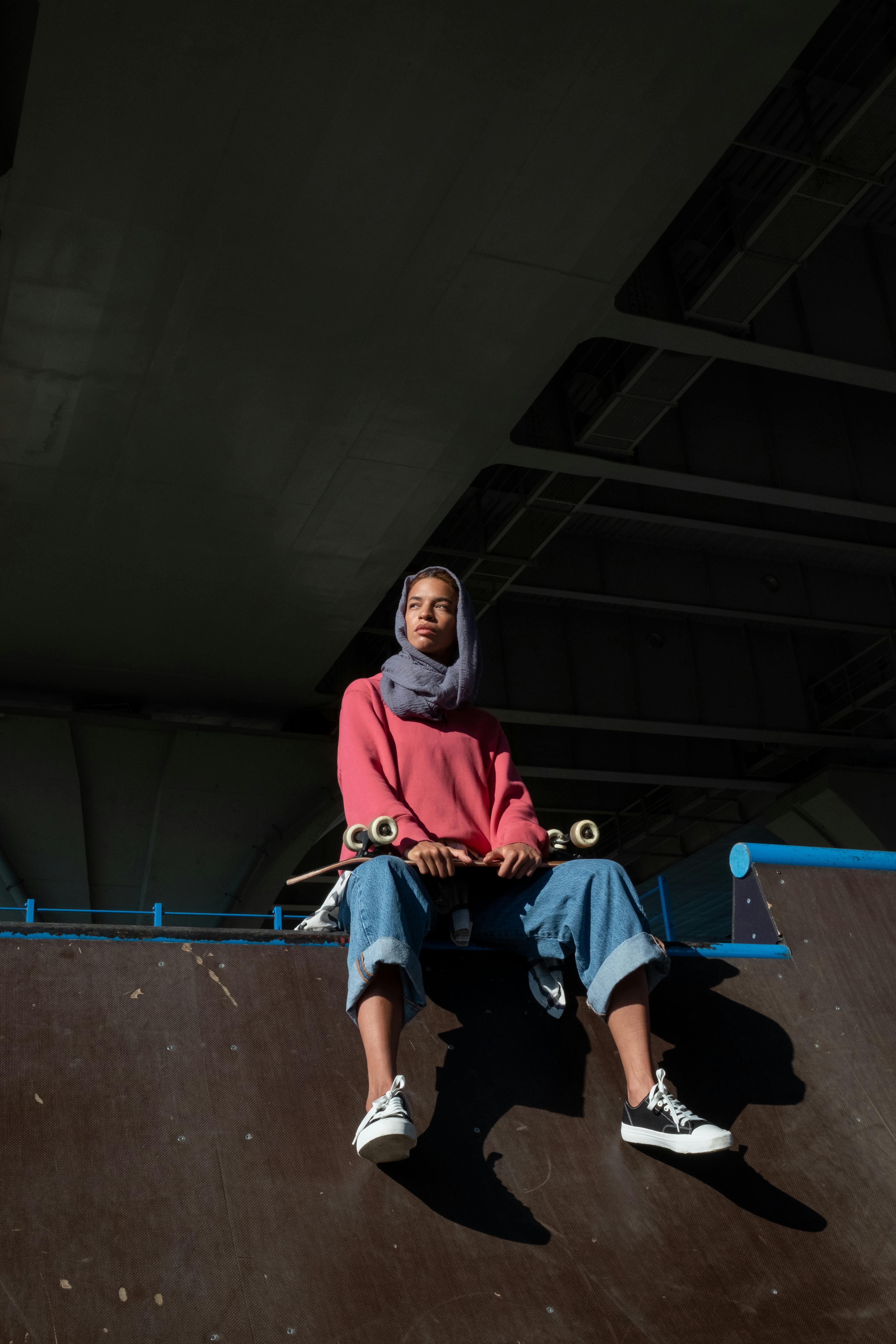 a woman sitting on a skate park while holding a skateboard
