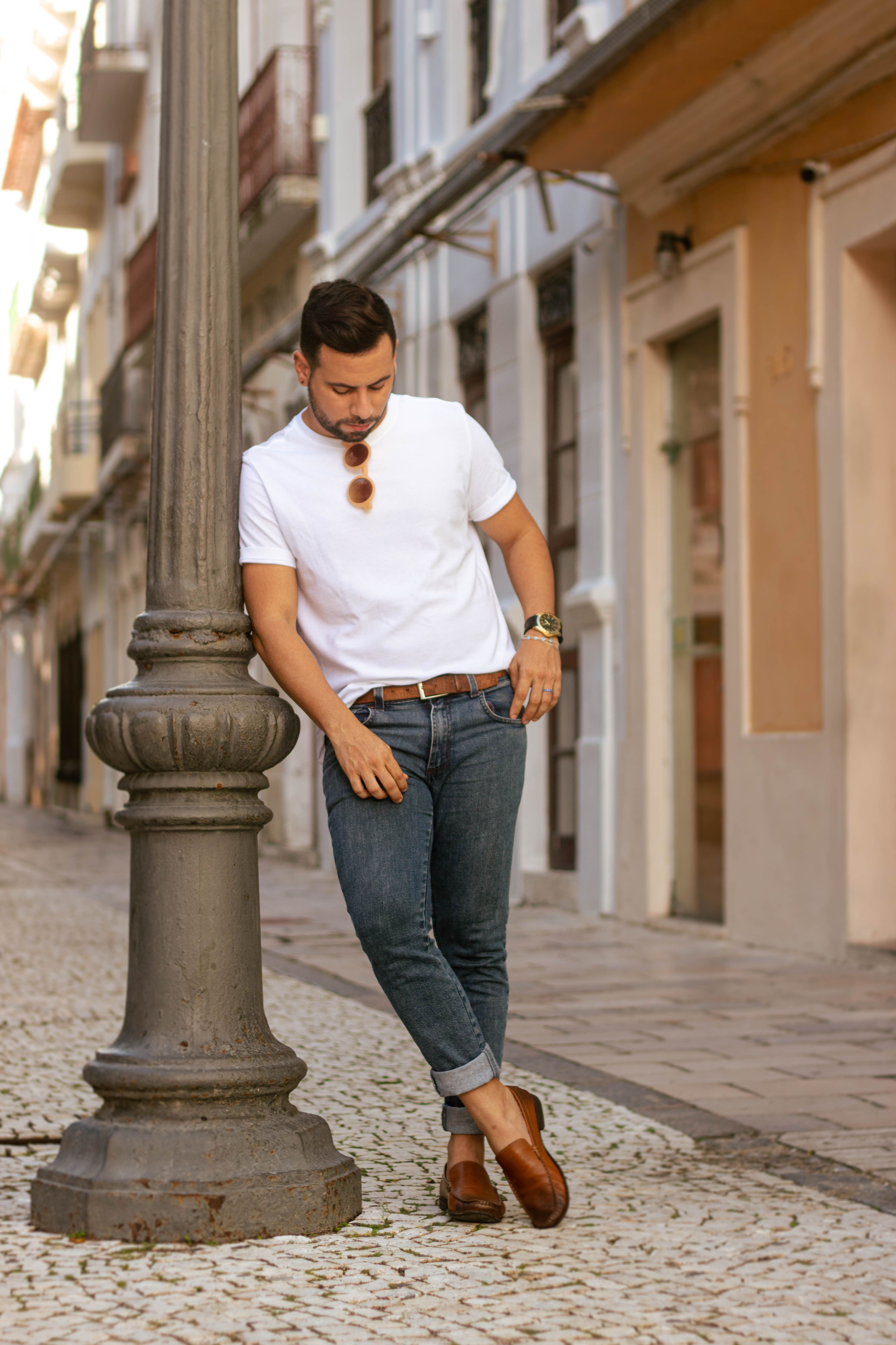 Casual man in jeans and tee leaning on lamppost in European street.