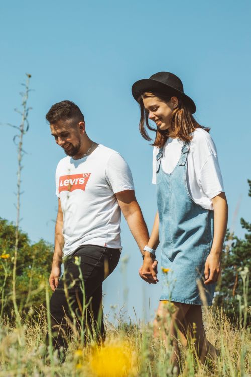Free A young couple holding hands while walking in a sunny field, enjoying a warm day. Stock Photo