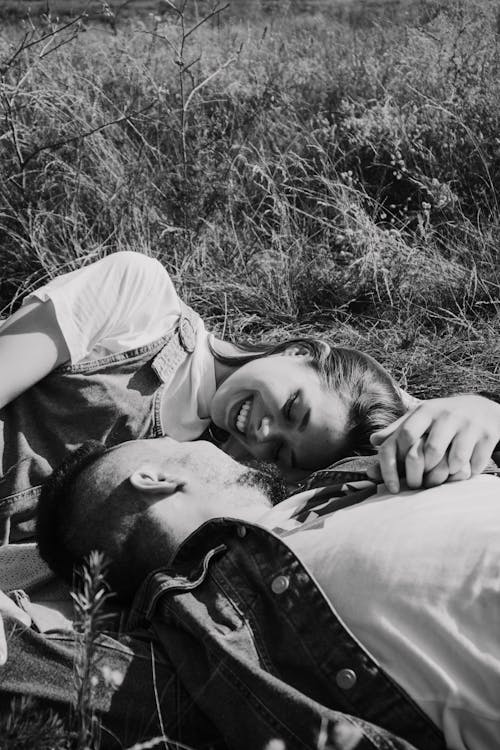 A Grayscale of a Couple Lying Down on a Field