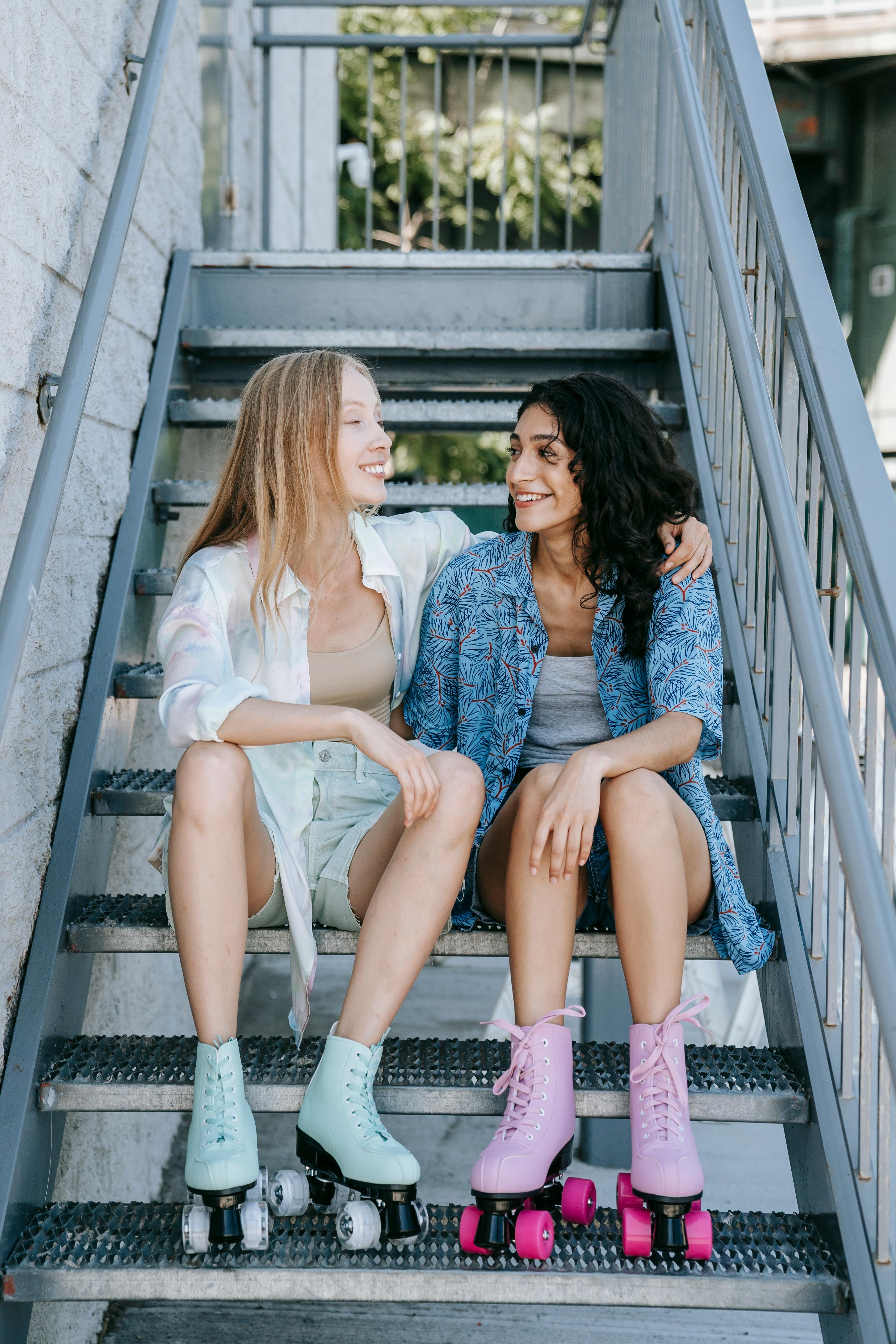 Two smiling women in roller skates sitting on stairs, enjoying summer day.