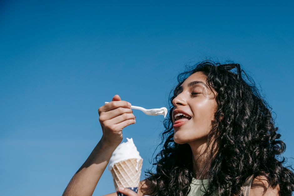A joyful woman savoring ice cream against a clear blue sky, capturing a summer moment.