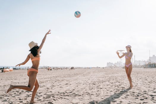 Two women enjoying a game of volleyball on a sandy beach under the sun.