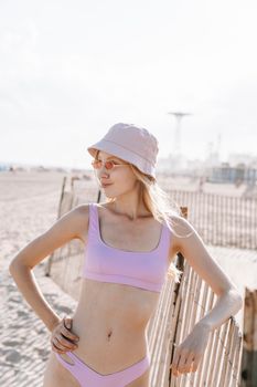 Stylish woman in pink bikini and hat poses confidently on a sunny beach day.
