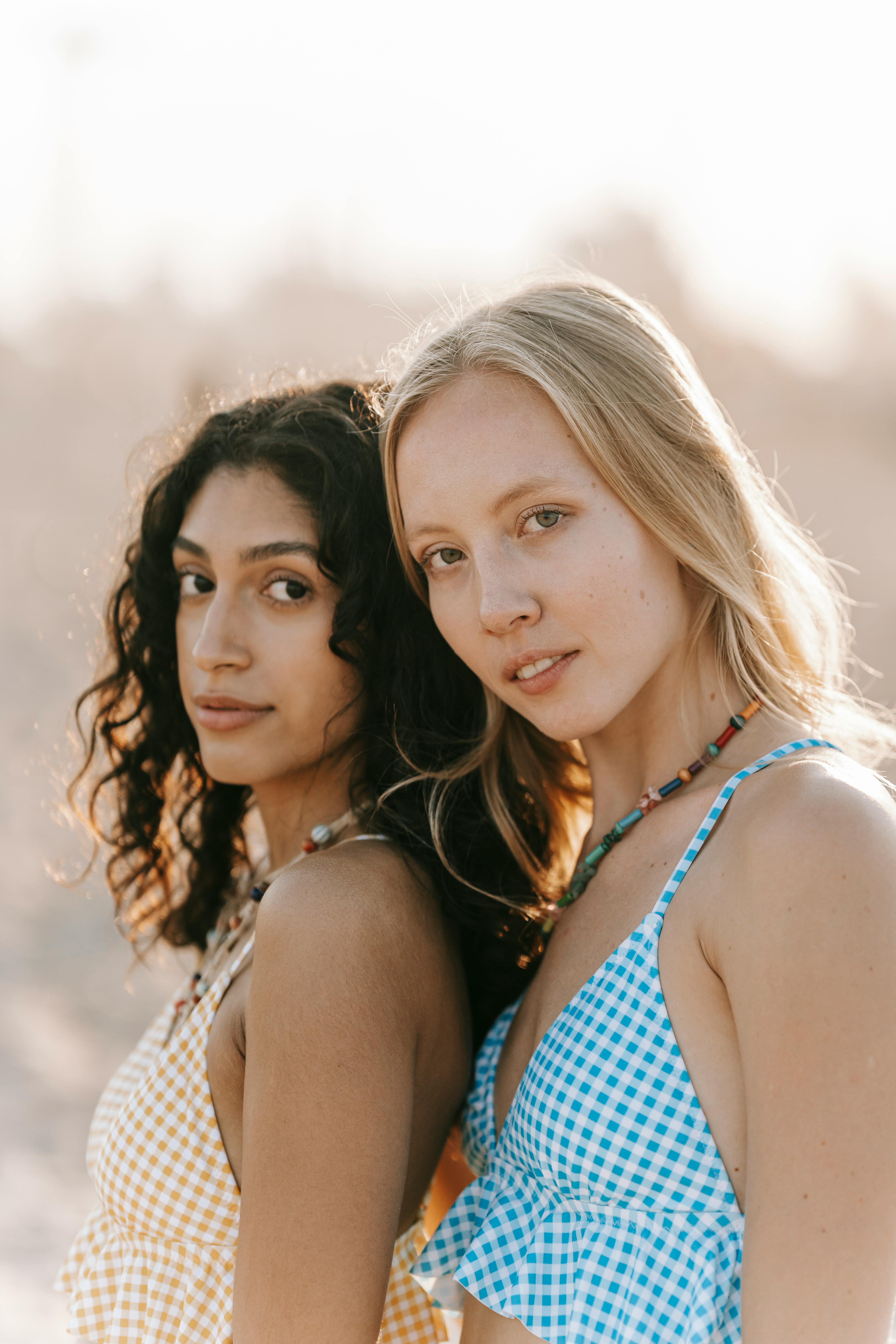 Two young women in summer attire pose together outdoors in bright sunlight.