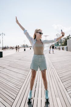 A cheerful young woman with arms spread, roller skating on a sunlit boardwalk.