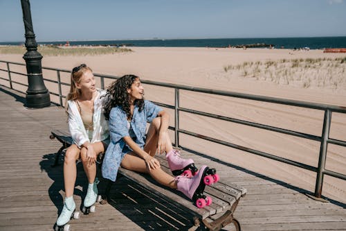 Young Women with Roller Skates Sitting on a Bench Near the Sea 