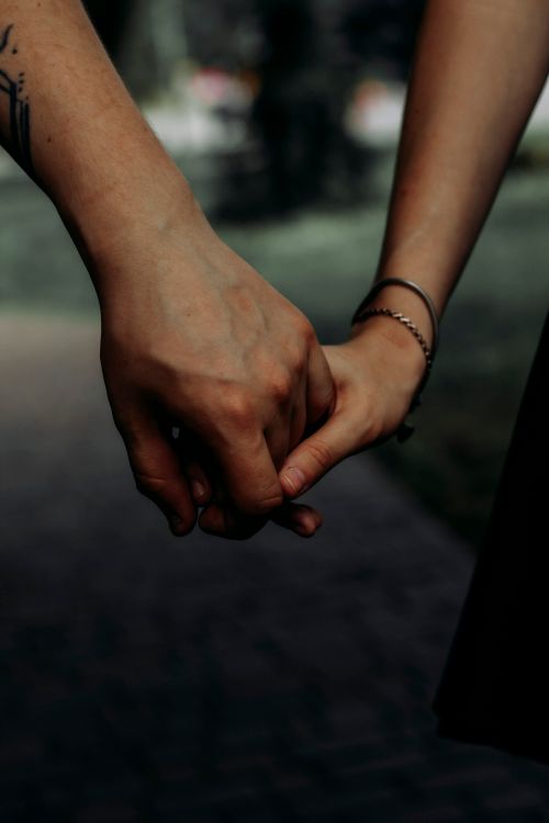 Free A close-up shot of two people holding hands in a dark and intimate setting. Stock Photo