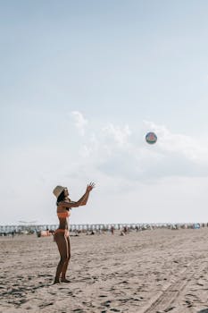 A woman in a bikini playing with a volleyball on a sunny beach.