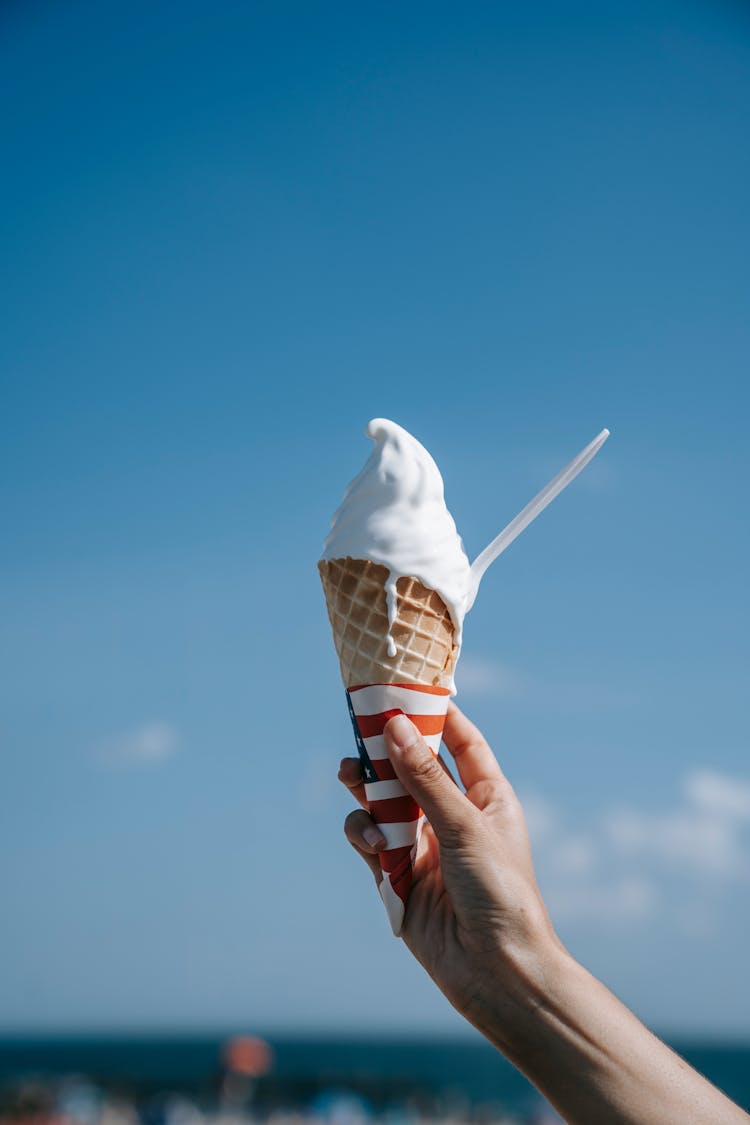 Person Hand Holding Ice Cream Against Blue Sky