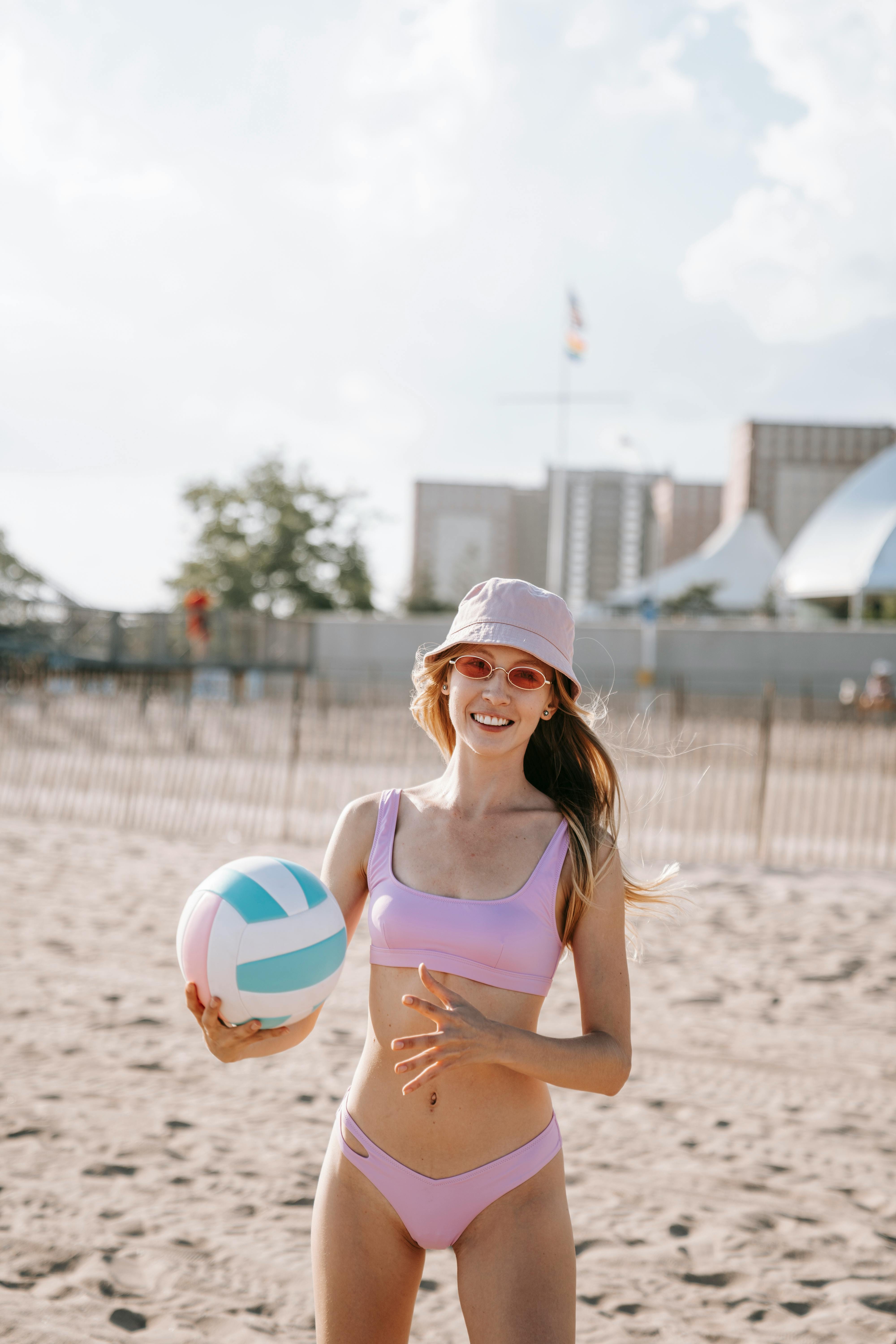 woman in purple bikini standing on beach sand holding a volleyball