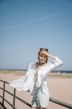 Young woman smiling on a breezy beach day, leaning on metal railings.