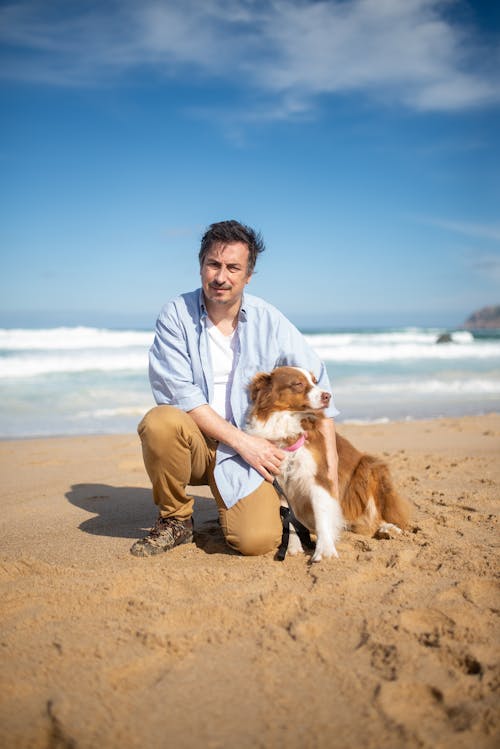 A Man Posing while Holding his Pet Dog Beside the Beach