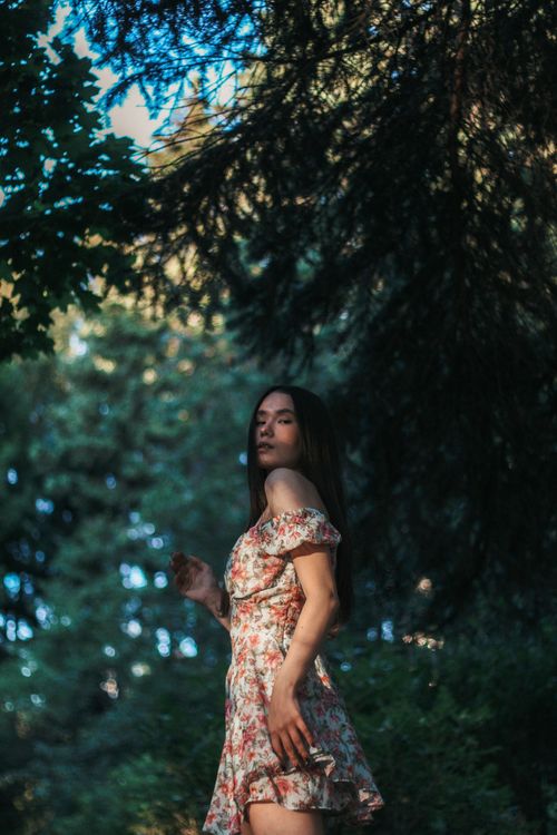 Free Young woman in a floral dress standing amidst lush greenery, exuding a serene vibe. Stock Photo