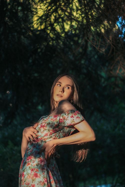 Free Elegant woman in a floral dress posing gracefully outdoors in natural lighting. Stock Photo