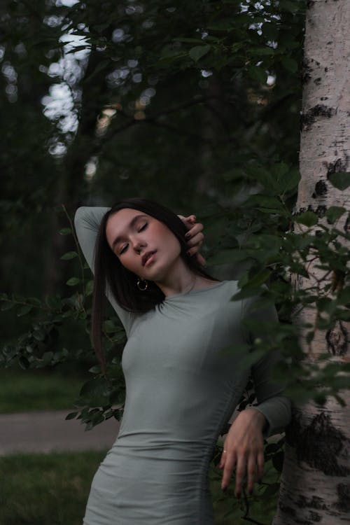 Dreamy woman tilting head to side while leaning on tree