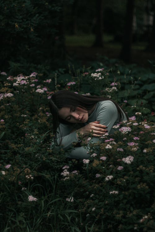 Young pensive woman sitting in blooming garden