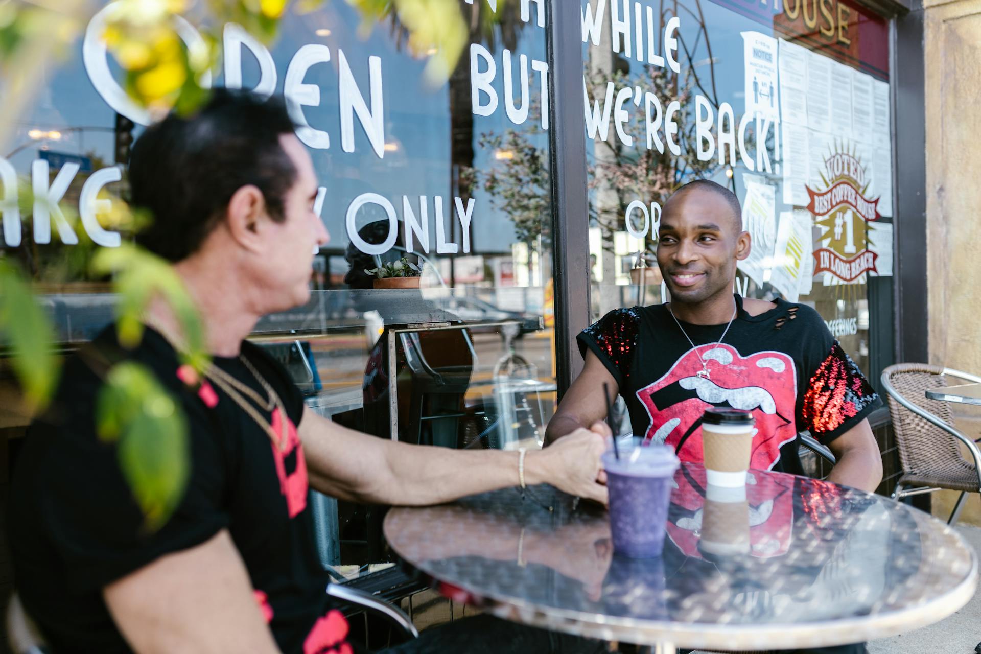 Two men enjoying coffee and conversation at an outdoor cafe table, bonding and laughing.