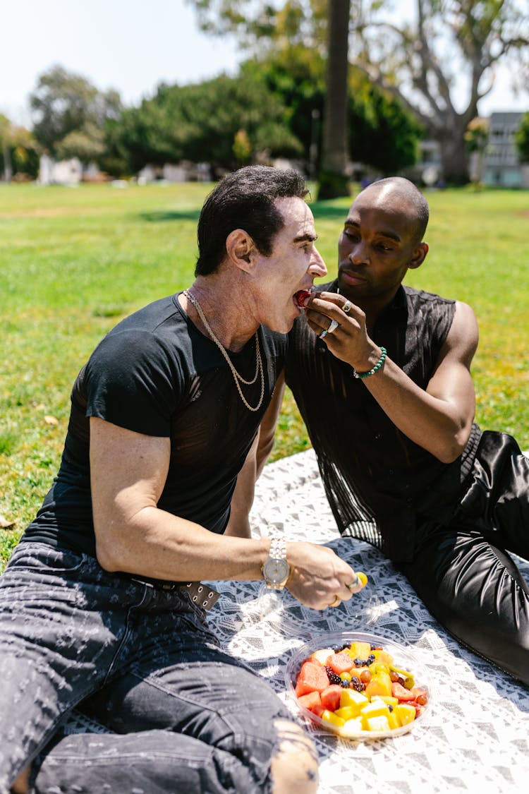 A Couple Eating Fruits While Sitting On The Grass