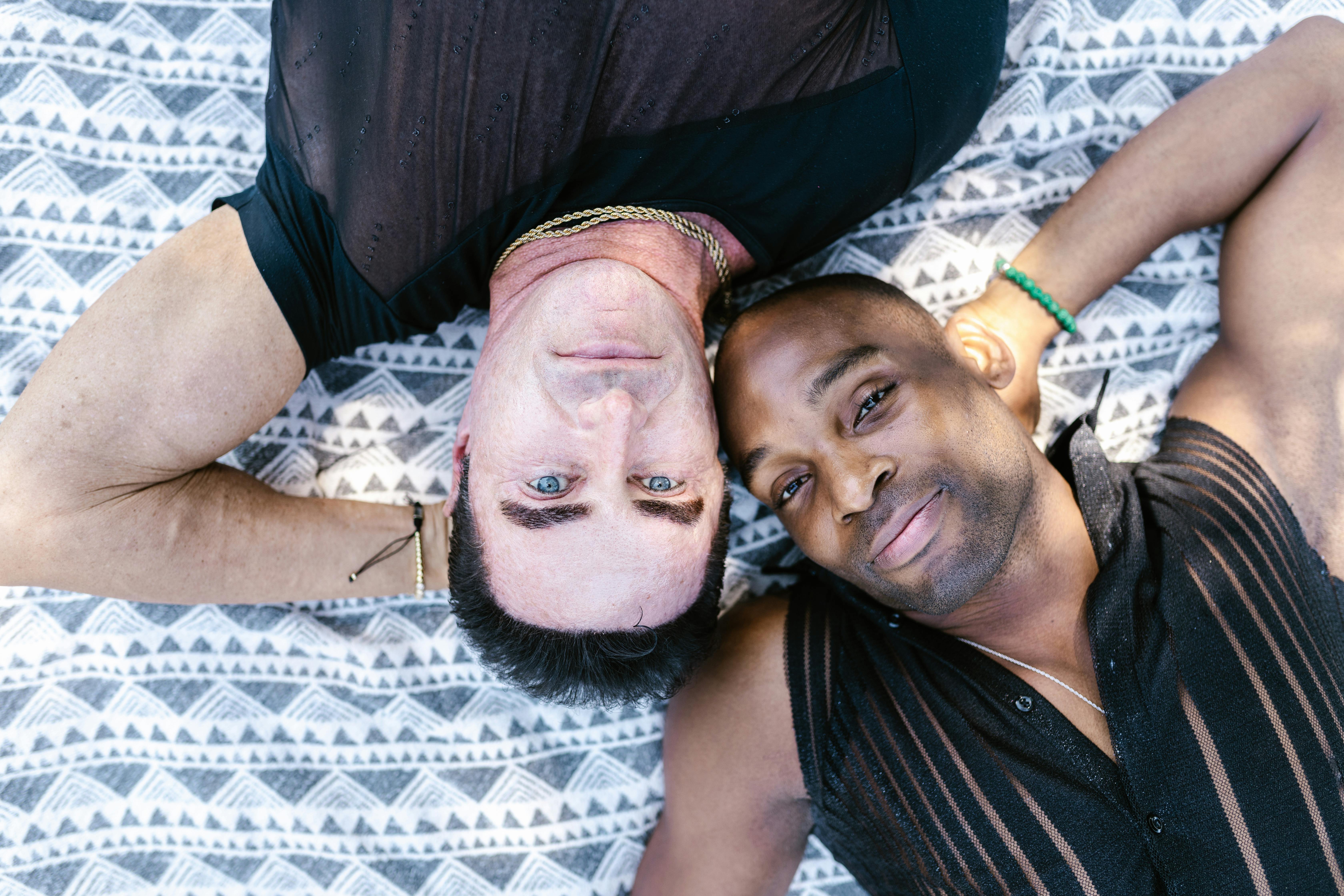 Portrait of interracial gay couple lying on blanket outdoors, smiling contently.