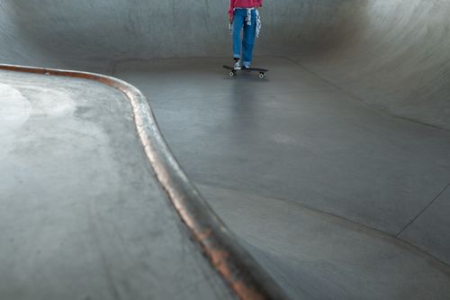 Free Skater riding a skateboard in a large concrete skatepark bowl on a sunny day. Stock Photo