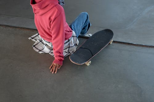 A Man in Red Hoodie Beside His Skateboard