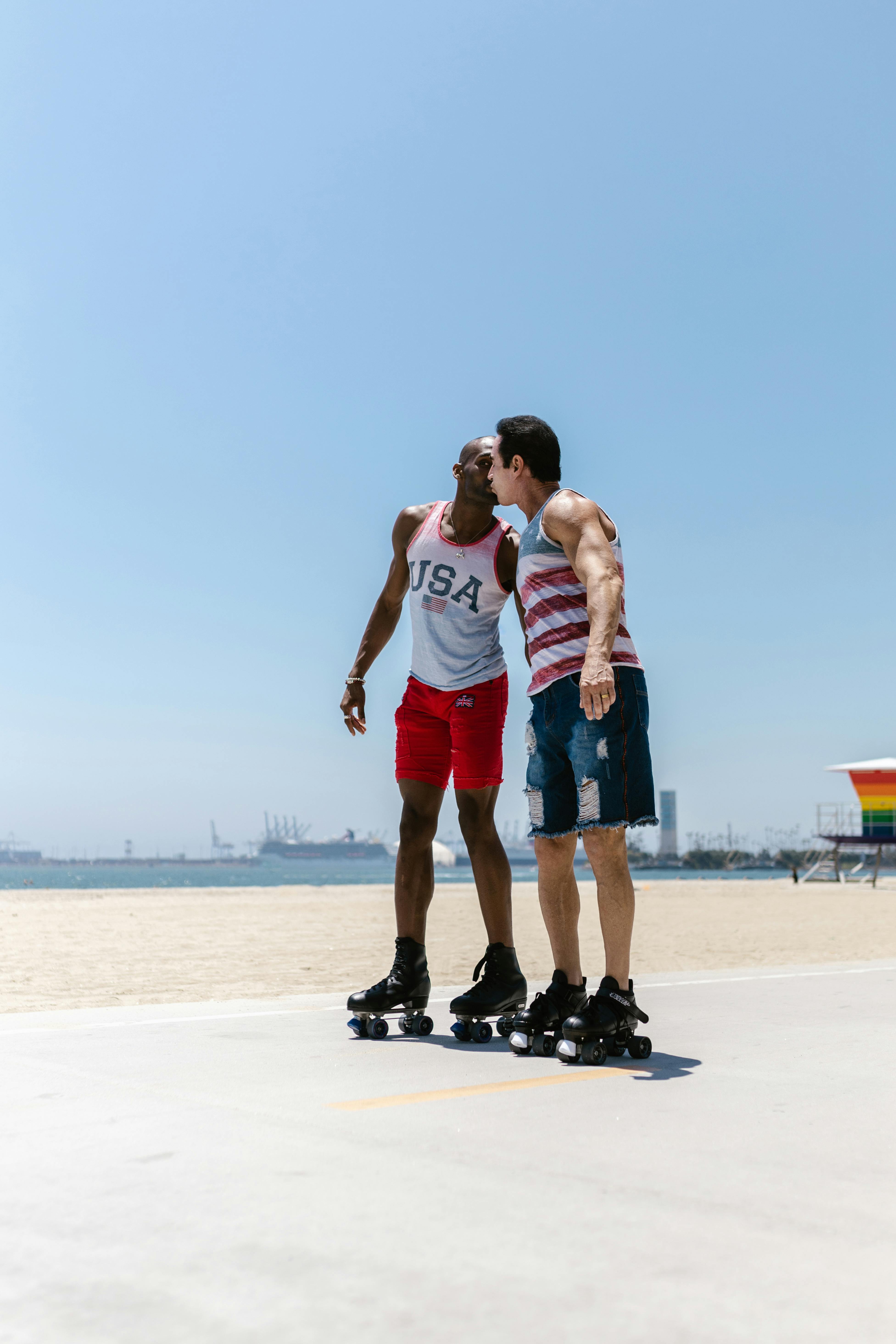 A loving gay couple sharing a kiss while roller skating on a sunny beach.